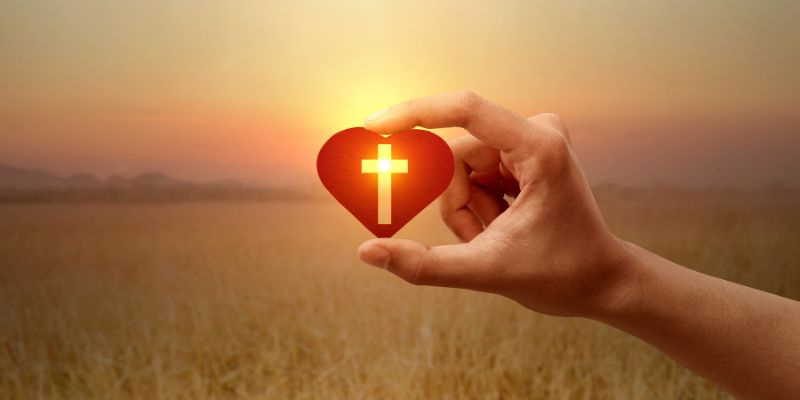 A heart symbol made with hands, with a cross in the background
