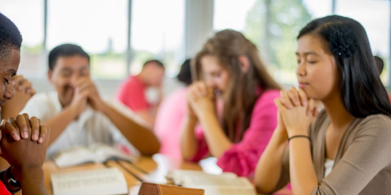 A Catholic teacher and students standing in prayer together